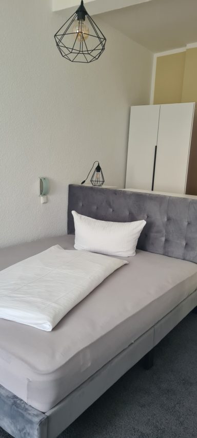 Moderne Wohnung mit grauem Bett, hellem Kopfteil und minimalistischer Dekoration.