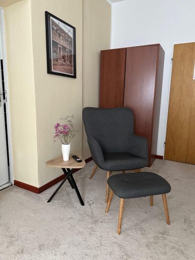 Grauer Sessel mit Fußhocker, Beistelltisch und Pflanze in einem Raum.