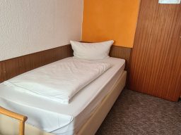 Helles Zimmer mit einem Doppelbett, orangefarbenem Sofa, einem Fernseher und Fenster mit Vorhängen.