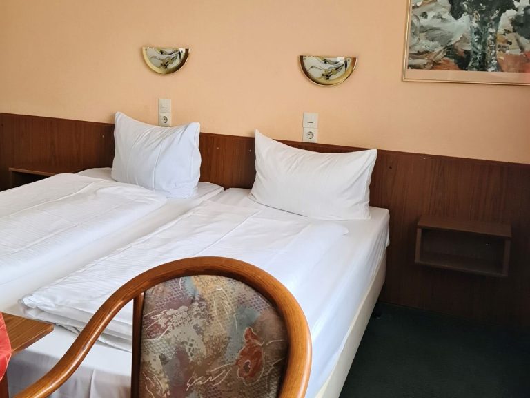 Zwei Betten mit weißen Bettdecken in einem einfachen Hotelzimmer.