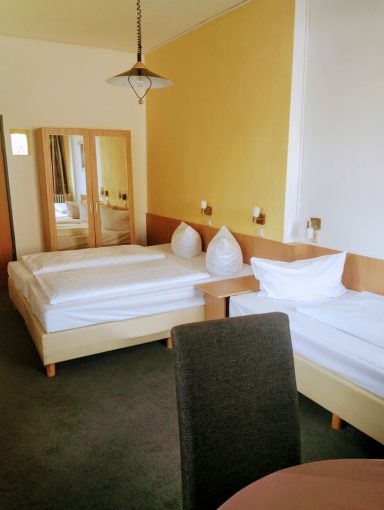 Helles Zimmer mit zwei Betten, Tisch und Spiegel, beige und gelbe Wände.