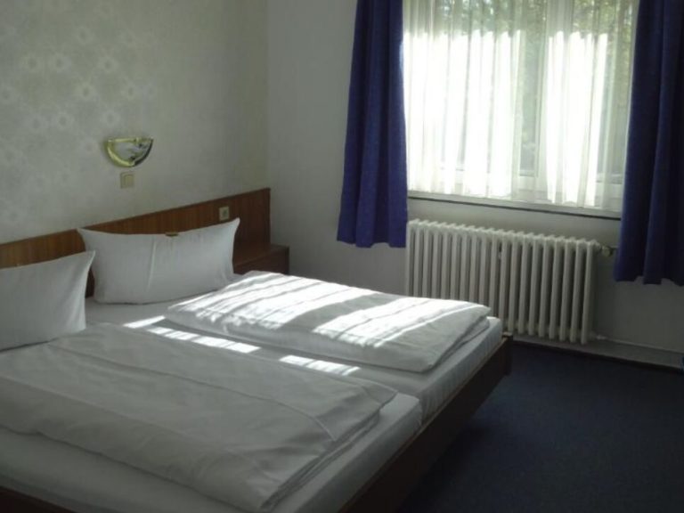 Helles Schlafzimmer mit zwei Betten, blauen Vorhängen und Tageslicht durch das Fenster.