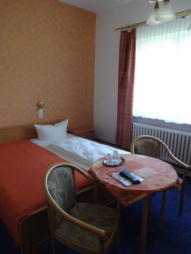 Gemütliches Zimmer mit einem Bett, Tisch, Stühlen und Fenster in warmen Farben.