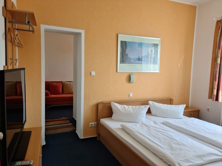 Beispiel Komfort Doppelzimmer Helles Hotelzimmer mit einem Doppelbett und einer angrenzenden Sitzecke.