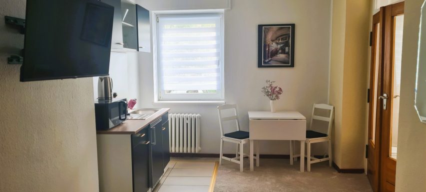 Moderne Küche mit Tisch und Stühlen, hellem Fenster und Kunstwerk an der Wand.