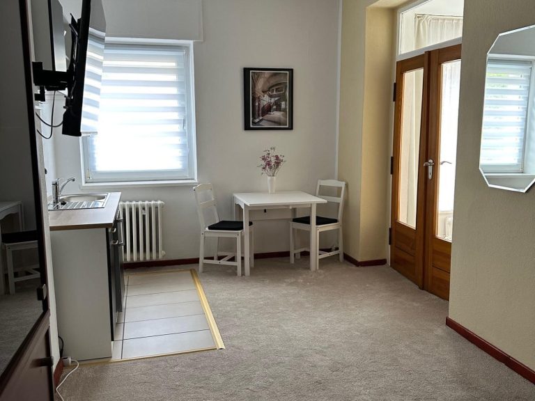 Beispiel Dreibettzimmer Helles Hotelzimmer mit drei Betten, Tisch, Stühlen und Fernseher.