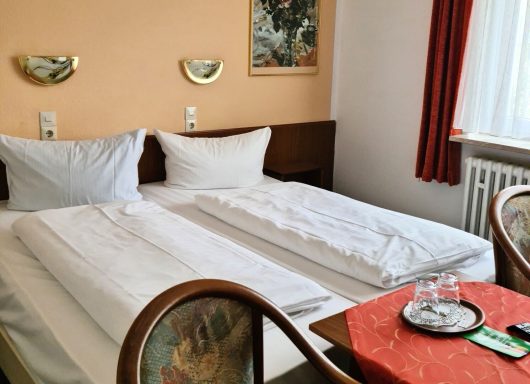 Zwei Einzelbetten in einem hellen Hotelzimmer mit einem Tisch und Fenster.
