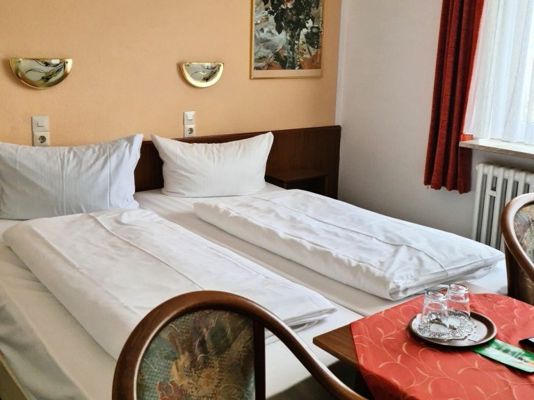 Doppelzimmer mit zwei Betten, Tisch und Fenster mit Vorhängen.