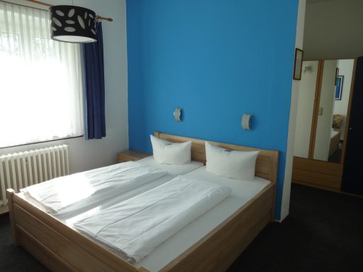 Helles Schlafzimmer mit zwei Betten, blauer Wand und Fenster mit Vorhängen.