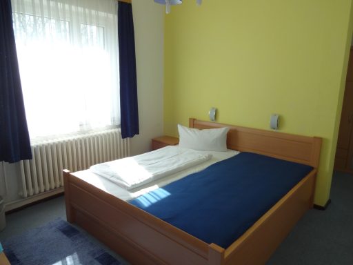 Helles Schlafzimmer mit Einzelbett, blauem Bettbezug und Vorhängen.