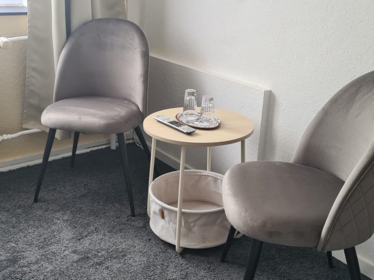 Zwei gepolsterten Stühle neben einem kleinen Tisch mit Wassergläsern und einem Korb.