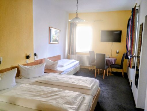 Helles Zimmer mit zwei Betten, einem Tisch und Fernseher, gemütlicher Atmosphäre.