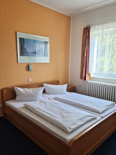 Ein helles Zimmer mit zwei Betten, orangefarbener Wand und großem Fenster.