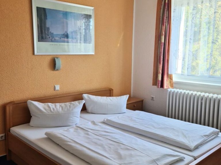 Beispiel Komfort Doppelzimmer Helles Zimmer mit zwei Einzelbetten, Holzmobiliar und einem großen Fenster.